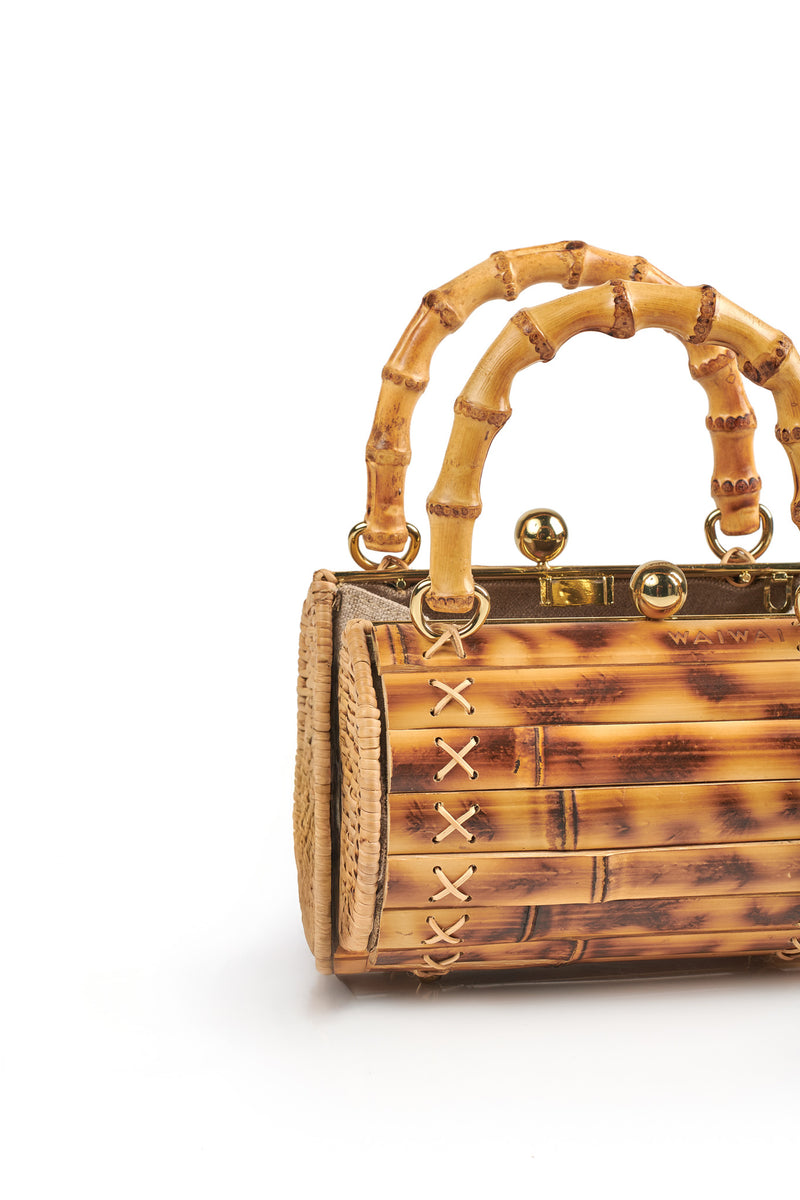 Bolsa de bambu rígida, com alça arredondada também em bambu, fecho dourado duplo e detalhe de costura cruzada nas laterais.