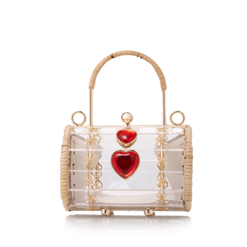 Bolsa cilíndrica em acrílico transparente com estrutura dourada revestida de vime e dois corações vermelhos aplicados.