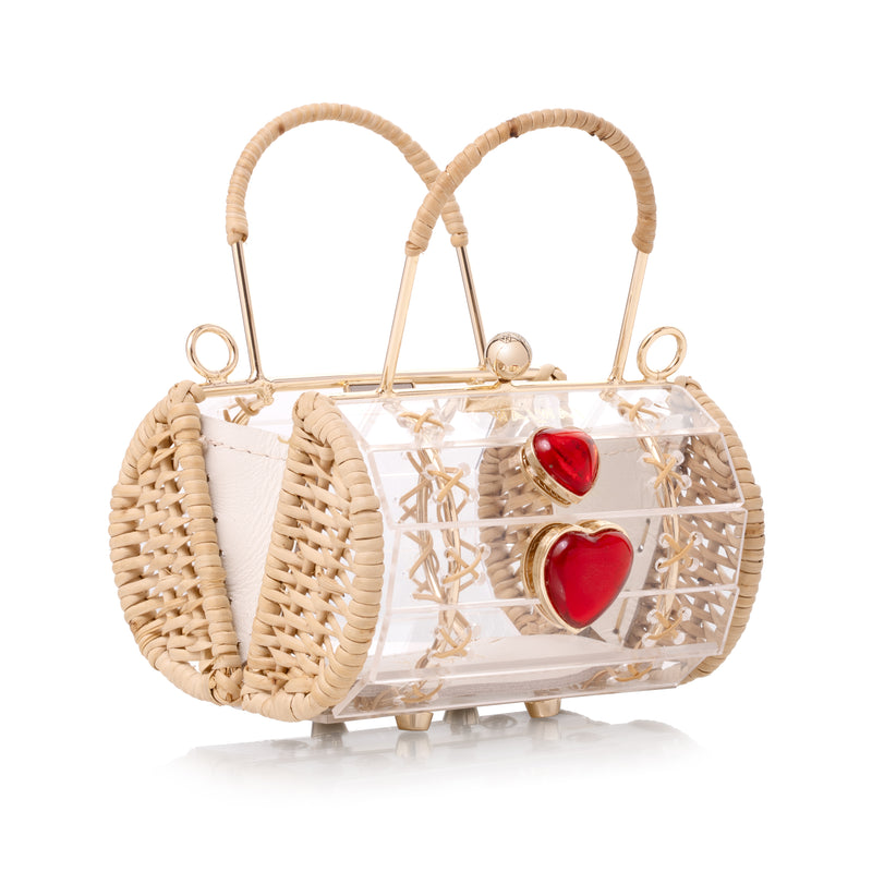 Bolsa de acrílico transparente com estrutura em metal dourado revestida de vime e detalhe central de corações vermelhos.