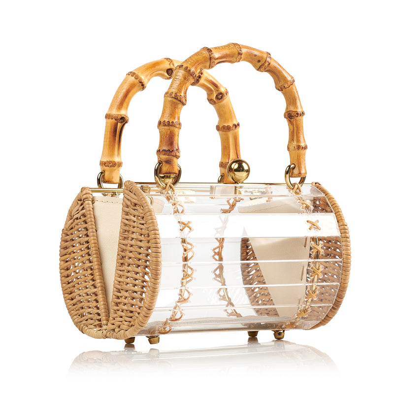 Bolsa box em acrílico transparente com laterais em rattan, detalhe de costura em X dourado, alça rígida em bambu e fecho esférico metálico dourado.