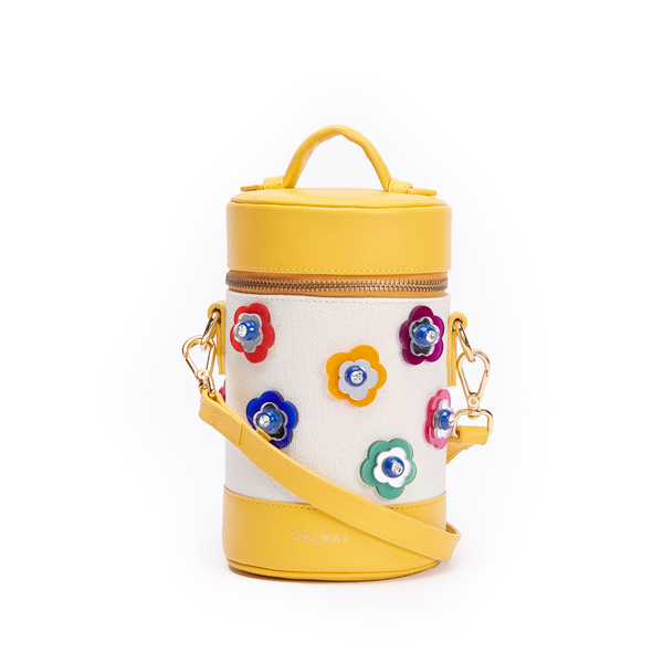 Bolsa cilíndrica em tecido bege com detalhes em couro amarelo. Alça longa removível e aplicações frontais de flores coloridas em relevo com miolo em cristal. Fechamento em zíper metálico dourado.