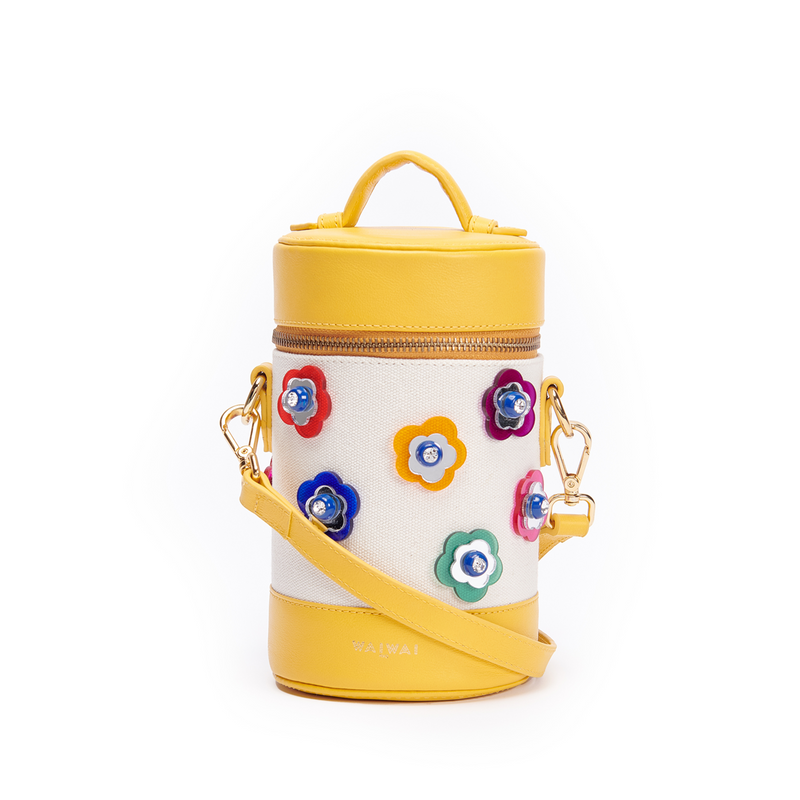 Bolsa cilíndrica em tecido bege com detalhes em couro amarelo. Alça longa removível e aplicações frontais de flores coloridas em relevo com miolo em cristal. Fechamento em zíper metálico dourado.