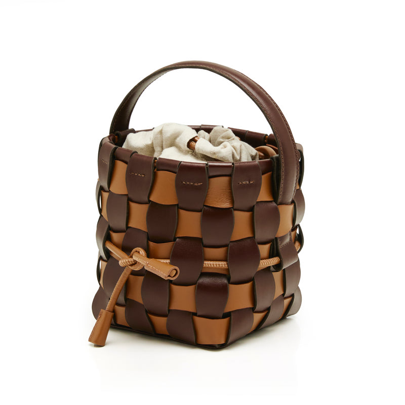 Bolsa bucket estruturada em couro trançado marrom e caramelo, com alça única e saquinho interno em tecido cru.