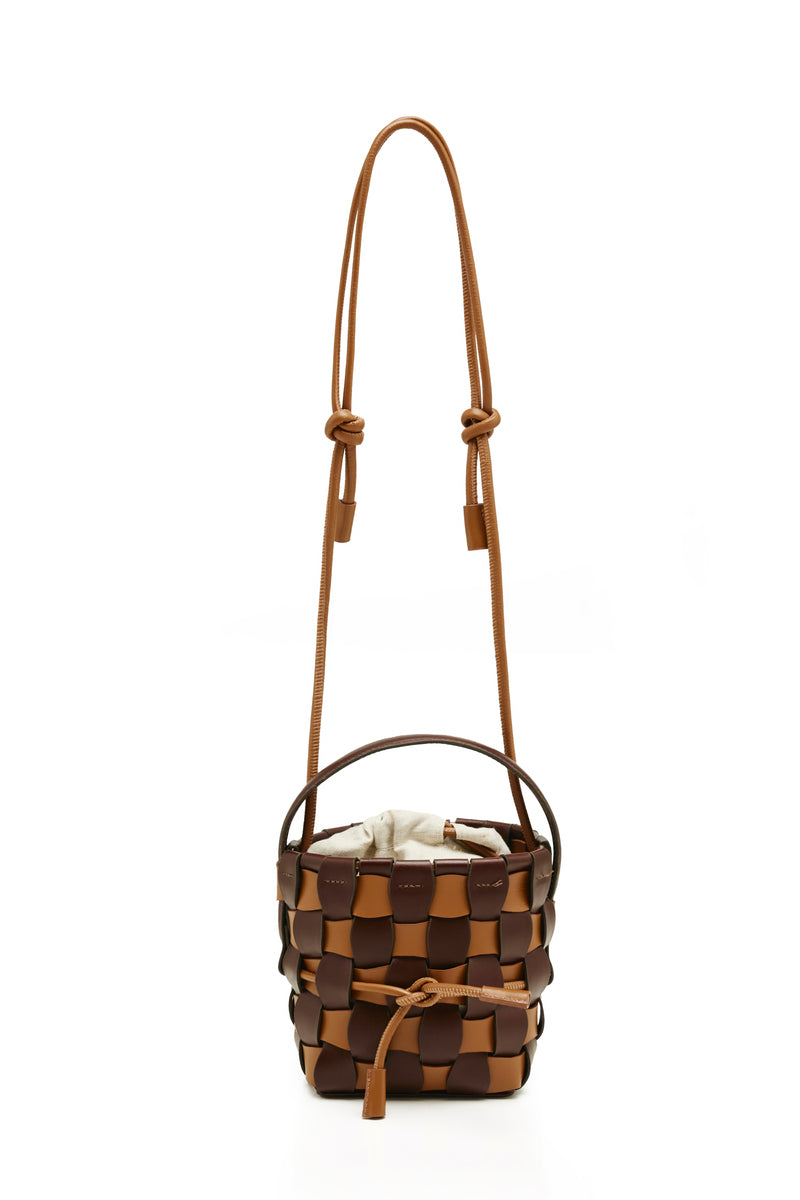 Bolsa bucket estruturada em couro trançado marrom e caramelo, com alça única e saquinho interno em tecido cru.