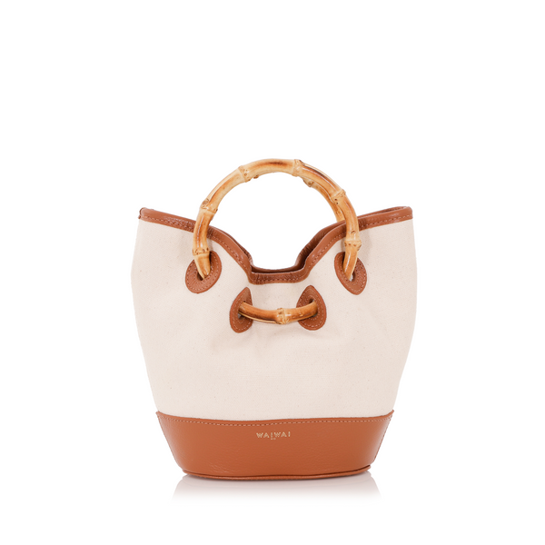 Bolsa bucket em linho cru com base e detalhes em couro caramelo, alça estruturada em bambu natural e fechamento por amarração.