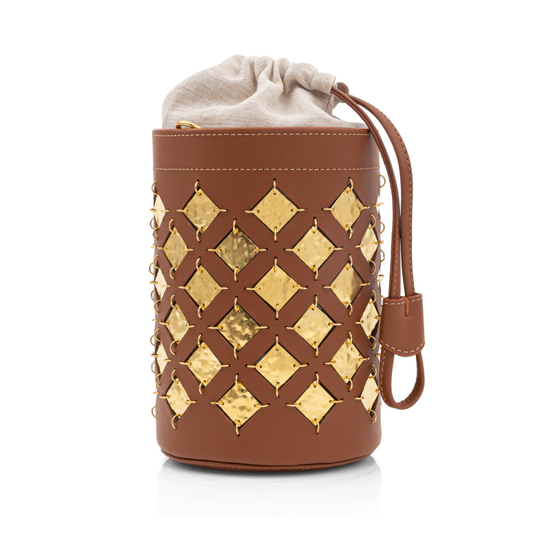 Bolsa bucket em couro marrom com aplicações geométricas quadradas em metal dourado. Possui alça tiracolo larga com recortes geométricos e fechamento superior com amarração interna.