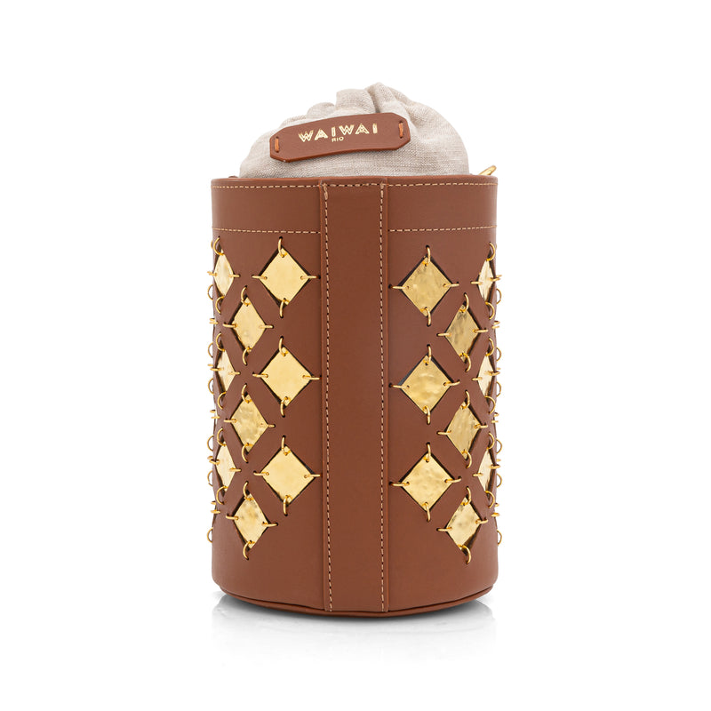 Bolsa bucket em couro marrom com aplicações geométricas quadradas em metal dourado. Possui alça tiracolo larga com recortes geométricos e fechamento superior com amarração interna.