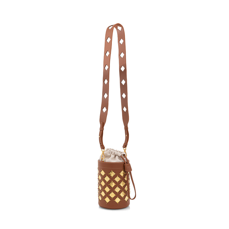 Bolsa bucket em couro marrom com aplicações geométricas quadradas em metal dourado. Possui alça tiracolo larga com recortes geométricos e fechamento superior com amarração interna.