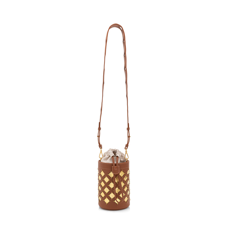 Bolsa bucket em couro marrom com aplicações geométricas quadradas em metal dourado. Possui alça tiracolo larga com recortes geométricos e fechamento superior com amarração interna.