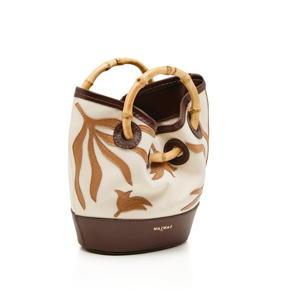 Bolsa bucket pequena em tecido cru com bordados marrons, base em marrom sólido e alça estruturada em bambu.