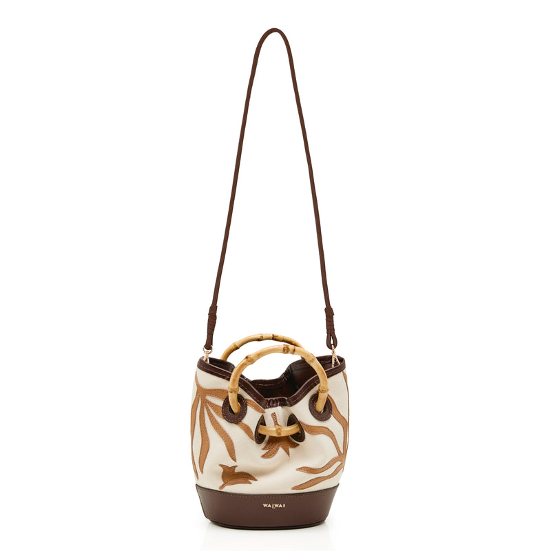 Bolsa bucket pequena em tecido cru com bordados marrons, base em marrom sólido e alça estruturada em bambu.