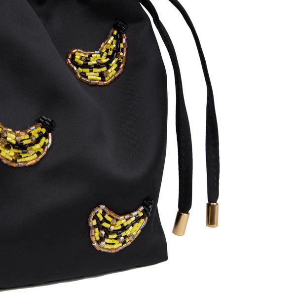Bolsa artesanal bucket em seda preta, bordada com bananas em cristais amarelos, alça de metal dourado com rattan e cordão ajustável.