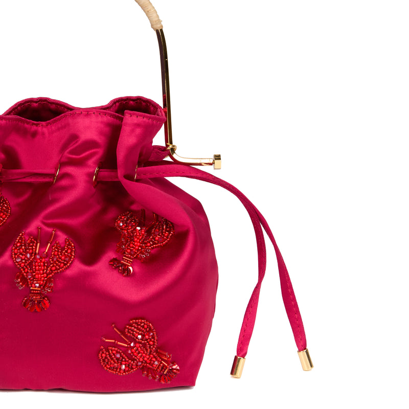 Bolsa artesanal bucket em seda rosa vibrante, bordada com lagostas de miçangas vermelhas, alça em metal dourado e fecho ajustável por cordão.