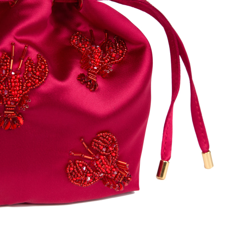Bolsa bucket luxuosa em seda rosa intensa, decorada com lagostas bordadas em miçangas vermelhas, alça estruturada dourada e detalhe em rattan.