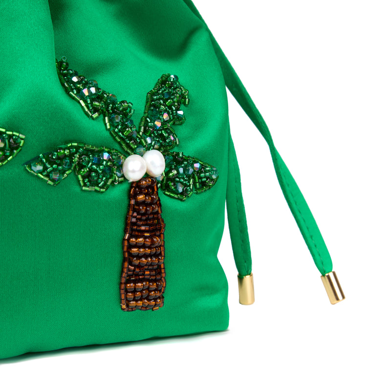 Bolsa bucket luxuosa em seda verde vibrante, com palmeiras bordadas em miçangas coloridas e pérolas, alça dourada estruturada e fecho de cordão.