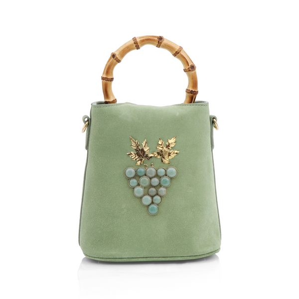 Bolsa bucket em camurça verde com alça de bambu e detalhe frontal de cacho de uvas formado por pedras verdes e folhas metálicas douradas.