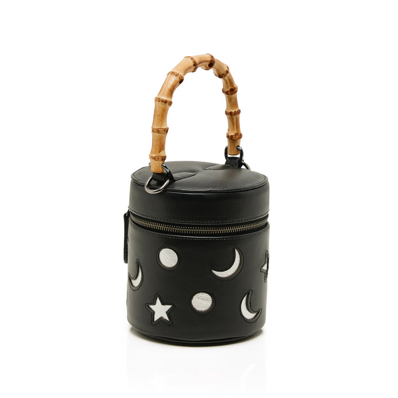 Bolsa cilíndrica preta em couro com bordados de luas e estrelas, fechamento em zíper e alça estruturada em bambu.