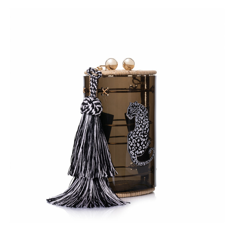 Bolsa clutch estruturada em acrílico preto translúcido, acabamento em rattan natural, estampa de onça branca central e franja longa em seda preta e branca, com fecho em esferas douradas.