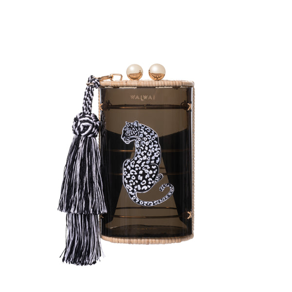 Clutch Waiwai em acrílico preto translúcido com estampa de onça branca central, fecho duplo em esferas douradas, acabamento em rattan e franja longa em seda preta e branca.