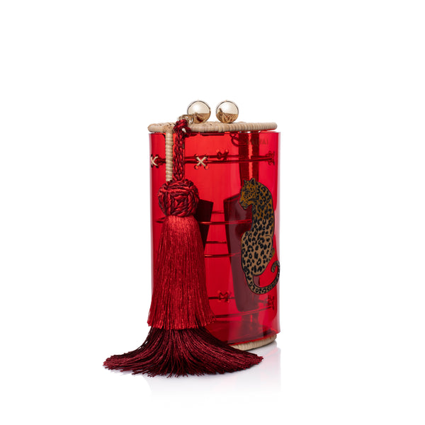 Clutch Waiwai em acrílico vermelho translúcido com estampa de onça central, fecho duplo em esferas douradas, acabamento em rattan e franja longa em seda vermelha.