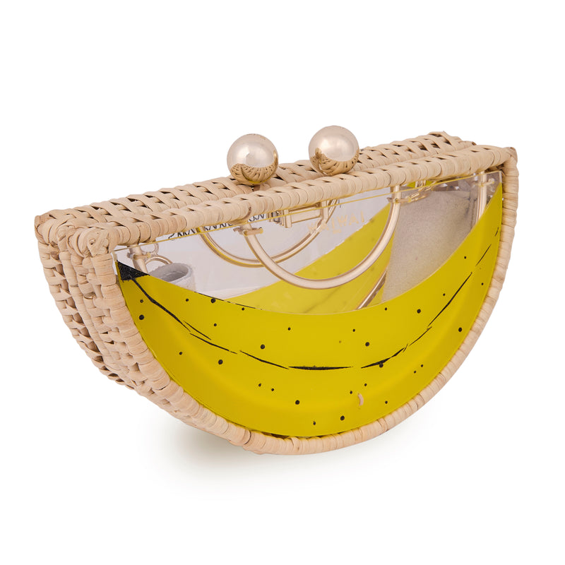 Clutch em formato meia-lua, feita em rattan e acrílico transparente, com estampa de banana amarela e fecho metálico dourado.