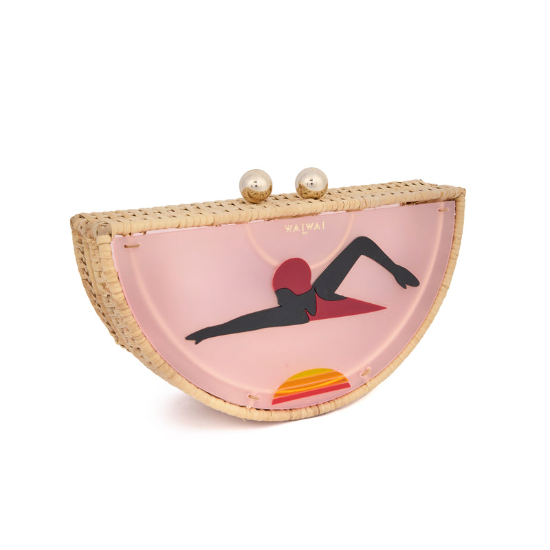 Clutch em formato meia-lua com estrutura em rattan e acrílico rosa translúcido, estampa estilizada de mulher deitada na praia com sol poente ao fundo, e fecho metálico dourado no topo.