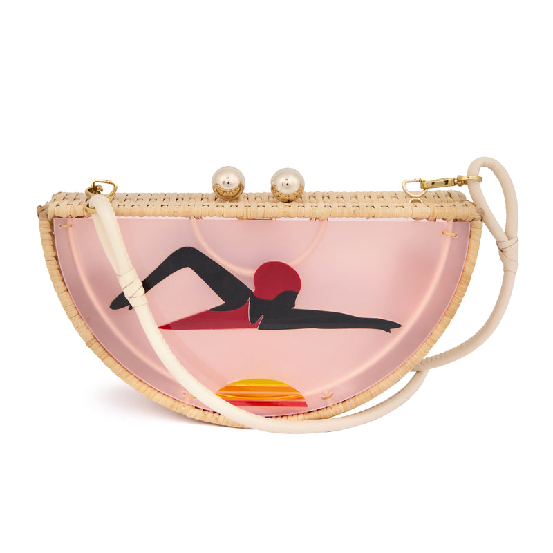 Clutch em formato meia-lua com estrutura em rattan e acrílico rosa translúcido, estampa estilizada de mulher deitada na praia com sol poente ao fundo, e fecho metálico dourado no topo.