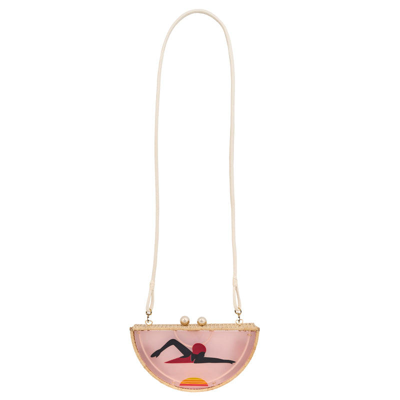 Clutch em formato meia-lua com estrutura em rattan e acrílico rosa translúcido, estampa estilizada de mulher deitada na praia com sol poente ao fundo, e fecho metálico dourado no topo.