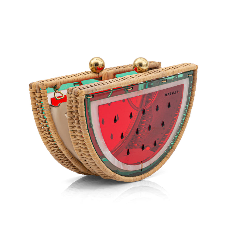 Clutch em formato de meia-melancia, feita em rattan e acrílico vermelho translúcido, com detalhes verdes, sementes pretas e fecho metálico dourado.