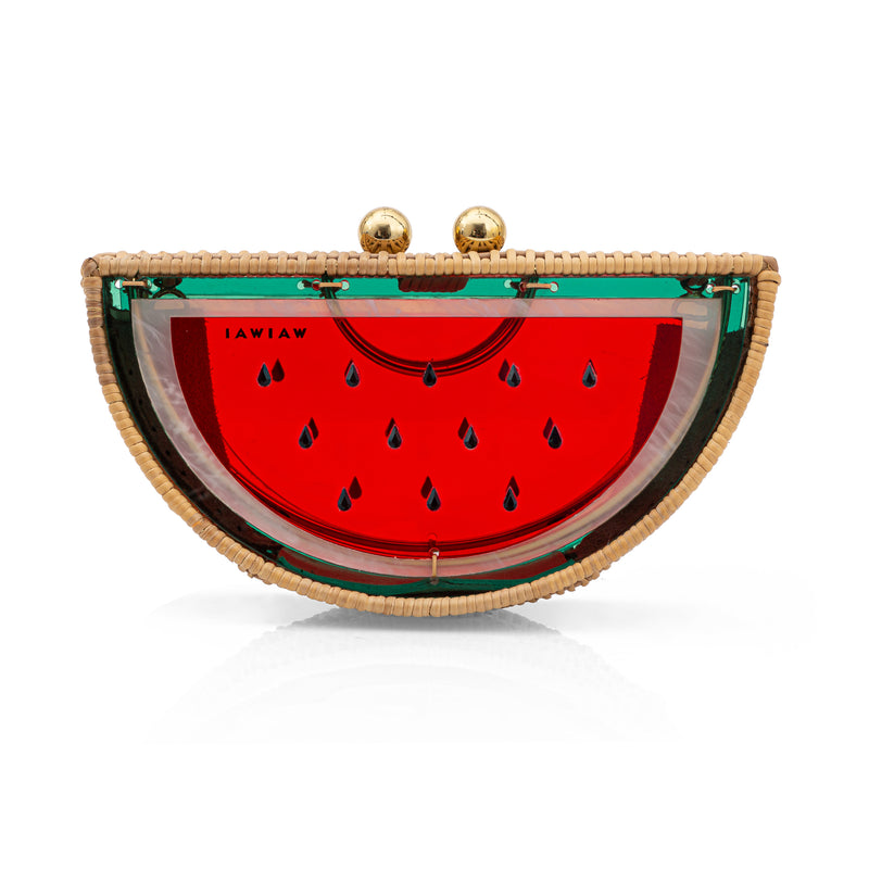 Clutch em formato meia-melancia, estruturada em rattan e acrílico vermelho translúcido, com detalhes verdes, sementes pretas e fecho dourado.