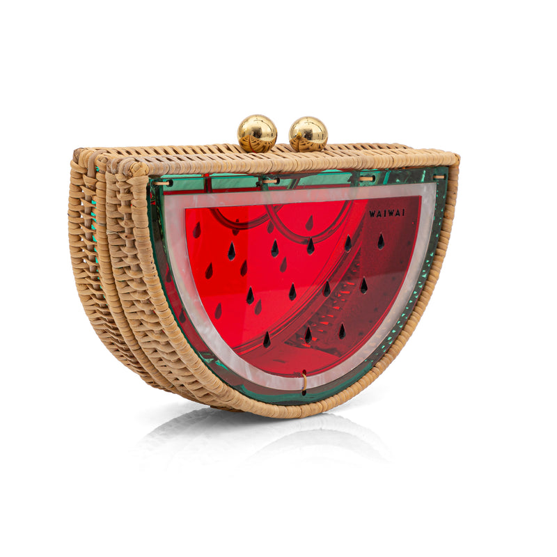 Bolsa clutch meia-melancia em rattan e acrílico vermelho translúcido, decorada com detalhes verdes, sementes pretas e fecho dourado superior.
