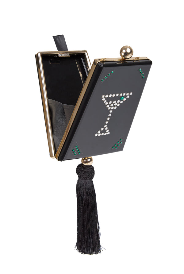 Clutch em veludo preto com aplicação central de taça formada por cristais, detalhes verdes nas bordas, fecho metálico dourado e franja longa em seda preta.