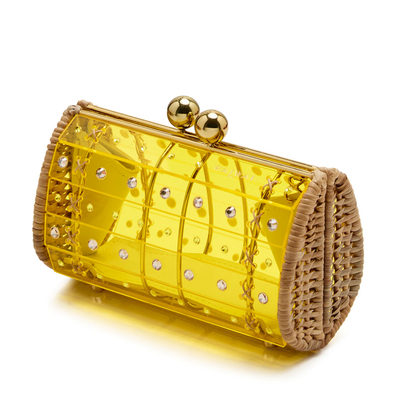 Clutch estruturada em rattan com corpo em acrílico amarelo translúcido, aplicação de cristais circulares e fecho metálico dourado no topo.