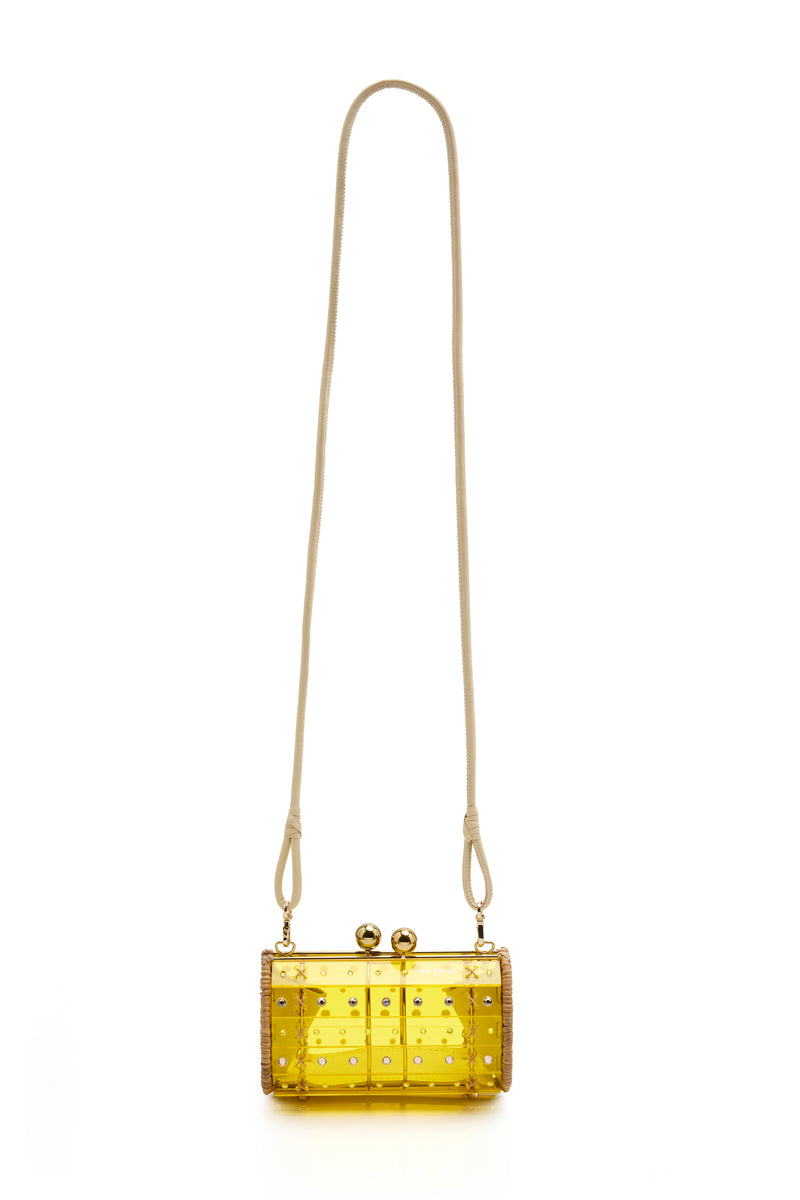 Clutch estruturada em rattan com corpo em acrílico amarelo translúcido, aplicação de cristais circulares e fecho metálico dourado no topo.