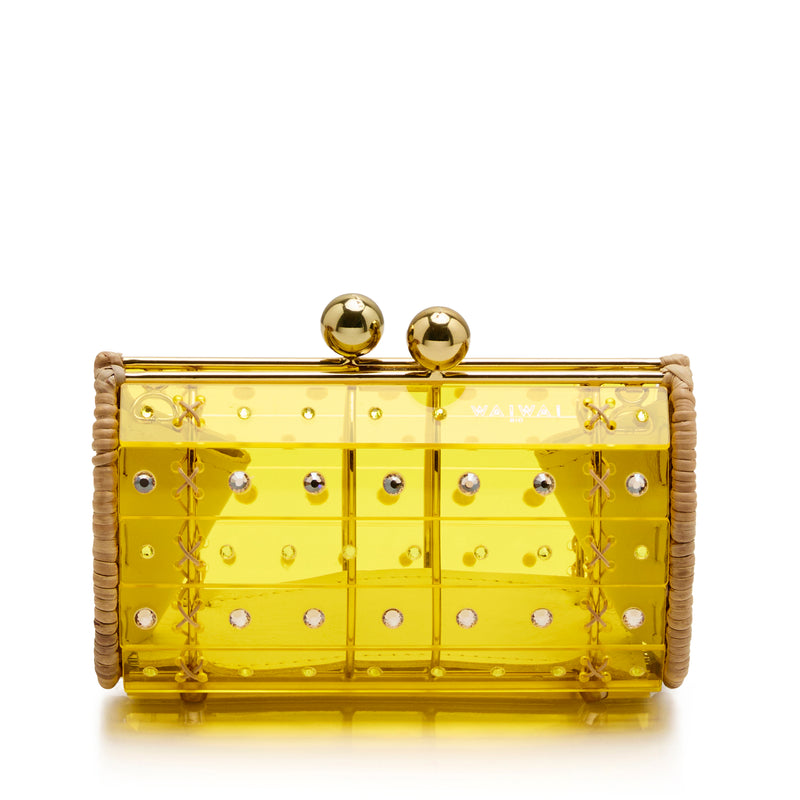 Clutch estruturada em rattan com corpo em acrílico amarelo translúcido, aplicação de cristais circulares e fecho metálico dourado no topo.