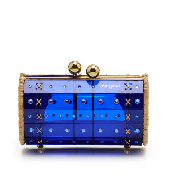Clutch estruturada em rattan com corpo em acrílico azul translúcido, aplicação de cristais circulares e fecho metálico dourado no topo, variação de ângulo frontal.