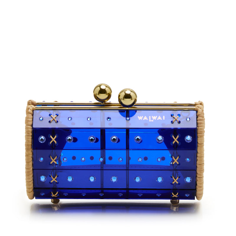 Clutch estruturada em rattan com corpo em acrílico azul translúcido, aplicação de cristais circulares e fecho metálico dourado no topo, variação de ângulo frontal.