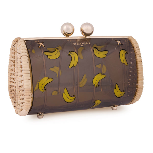Bolsa clutch artesanal em rattan natural, com corpo em acrílico preto translúcido, decorada com bananas amarelas e fecho metálico dourado.