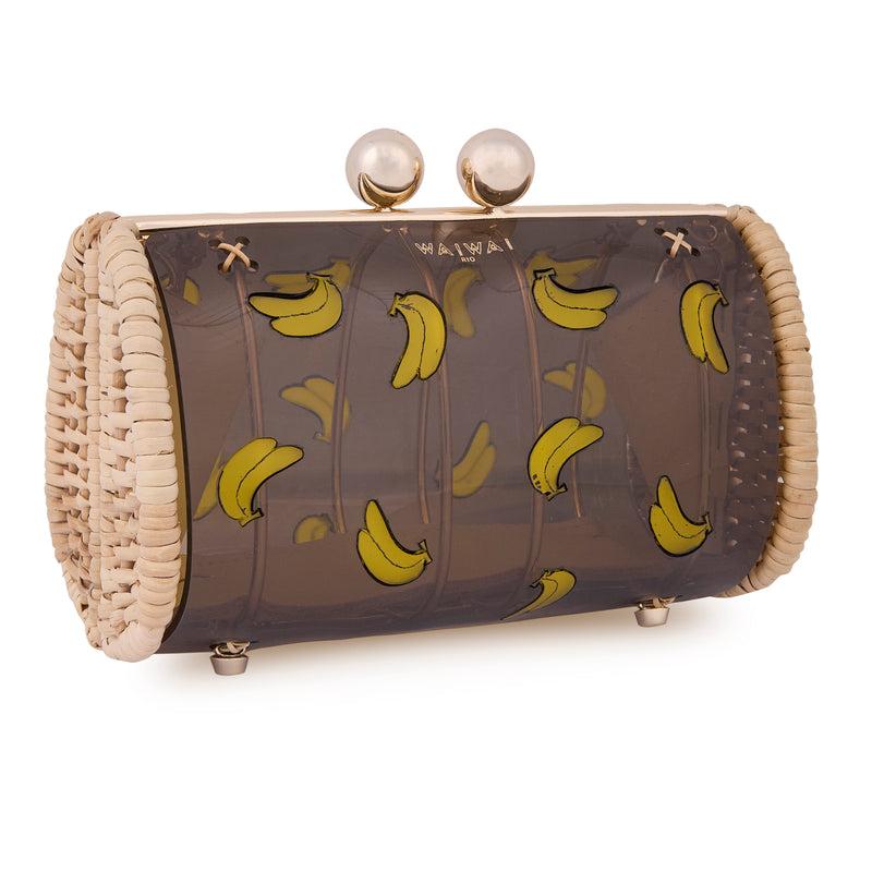 Bolsa clutch artesanal em rattan natural, com corpo em acrílico preto translúcido, decorada com bananas amarelas e fecho metálico dourado.
