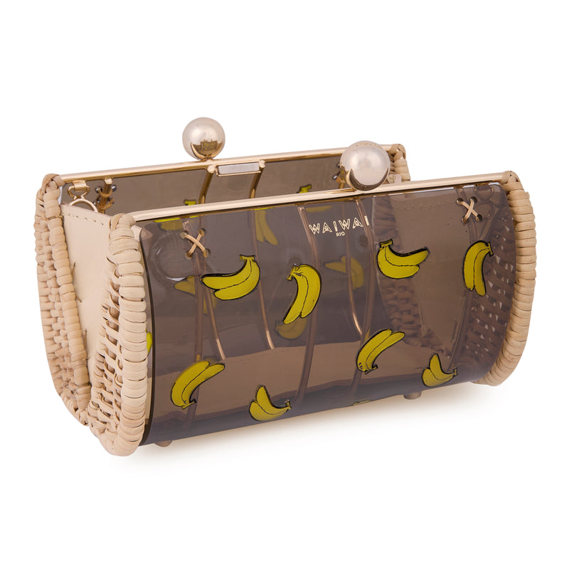 Clutch autoral em rattan e acrílico preto translúcido, frente estampada com várias bananas amarelas e fecho dourado.