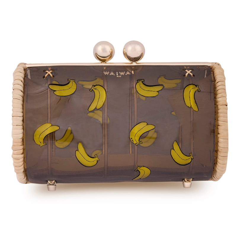 Clutch estruturada em rattan com corpo em acrílico preto translúcido, estampa divertida de várias bananas amarelas e fecho metálico dourado no topo.