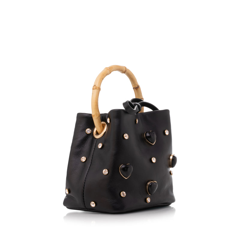 Bolsa pequena preta em couro, com corações dourados aplicados e alça estruturada em bambu natural.