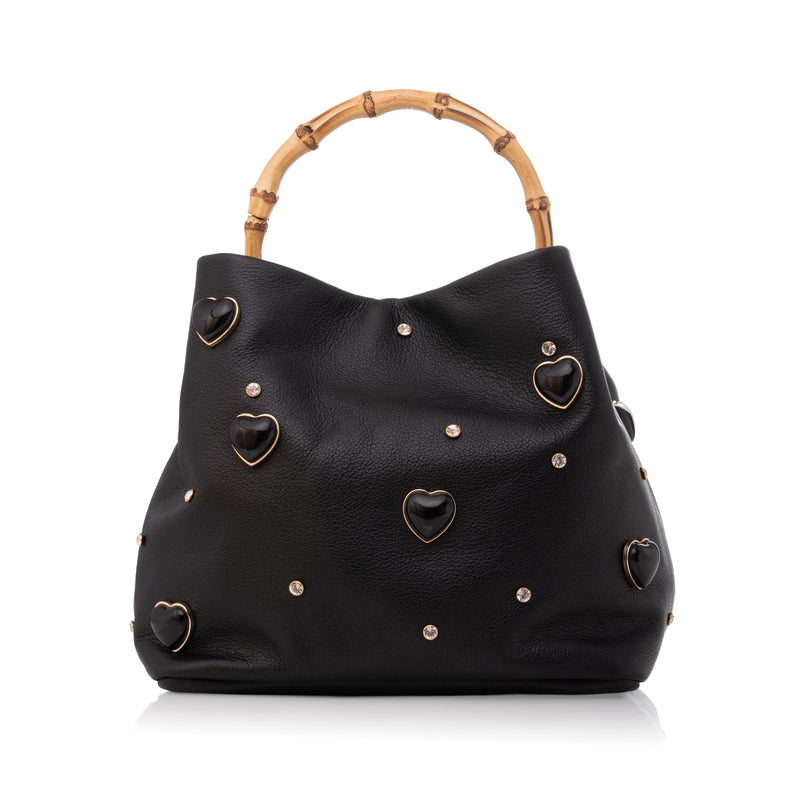 Bolsa grande em couro preto com aplicações de corações dourados e alça superior em bambu natural.