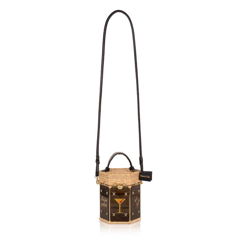 Bolsa hexagonal estruturada em rattan e acrílico preto translúcido, com estampa de taça de cocktail dourada com cereja vermelha ao centro, alça curta em couro preto e fecho metálico dourado.