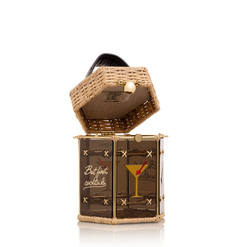Bolsa hexagonal estruturada em rattan e acrílico preto translúcido, com estampa de taça de cocktail dourada com cereja vermelha ao centro, alça curta em couro preto e fecho metálico dourado.