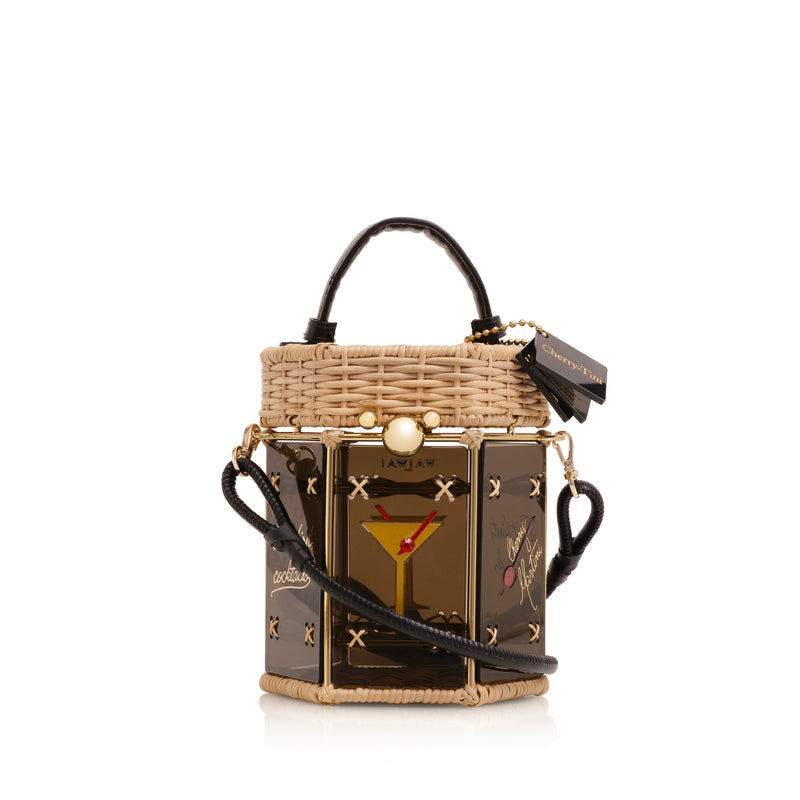 Bolsa hexagonal estruturada em rattan e acrílico preto translúcido, com estampa de taça de cocktail dourada com cereja vermelha ao centro, alça curta em couro preto e fecho metálico dourado.