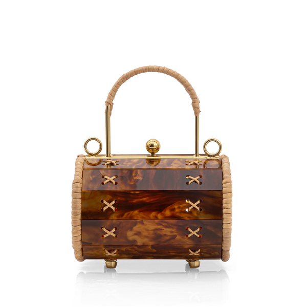 Bolsa pequena estruturada em resina tartaruga com laterais em palha natural, fecho esférico dourado e alça rígida revestida em palha. Detalhes de amarrações artesanais em X nas laterais.