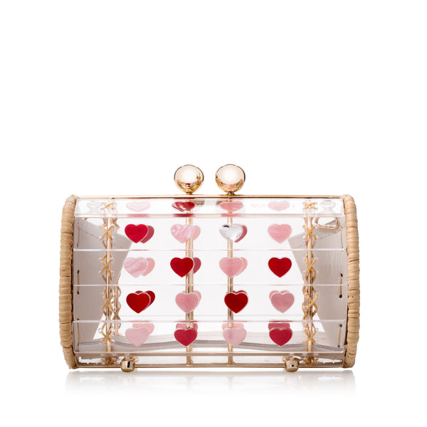 Bolsa cilíndrica em acrílico transparente com estrutura dourada revestida de vime e aplicações de corações vermelhos e rosas.