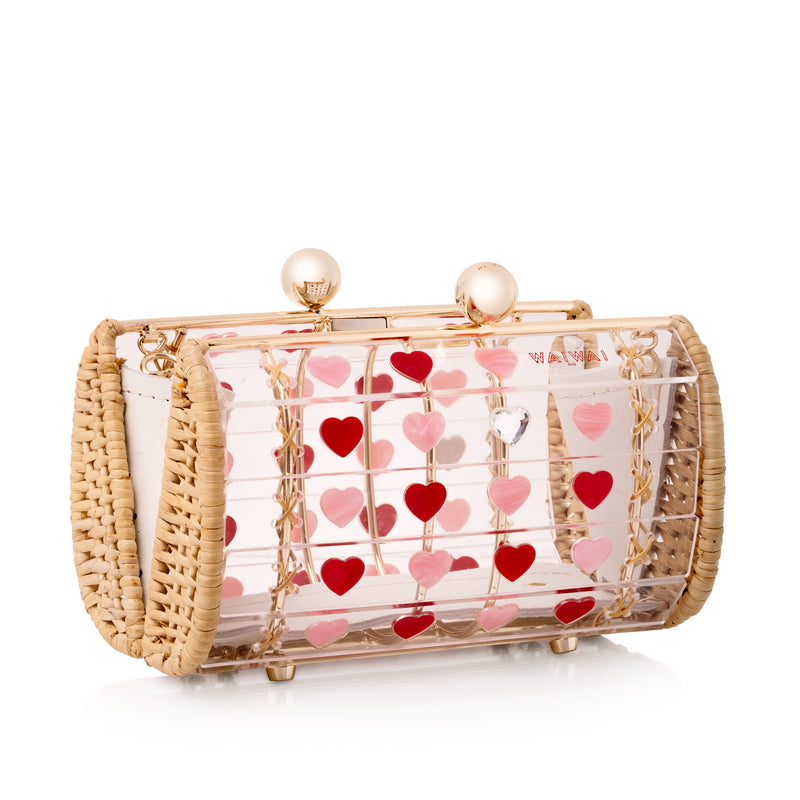 Bolsa de acrílico transparente com estrutura em metal dourado revestida de vime e estampa de corações vermelhos e rosas.