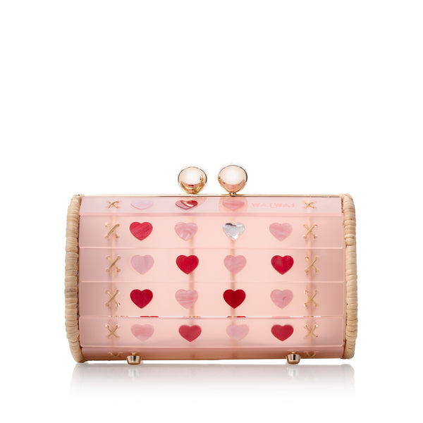 Bolsa cilíndrica em acrílico rosa translúcido com estrutura dourada revestida de vime e aplicações de corações vermelhos e rosas.